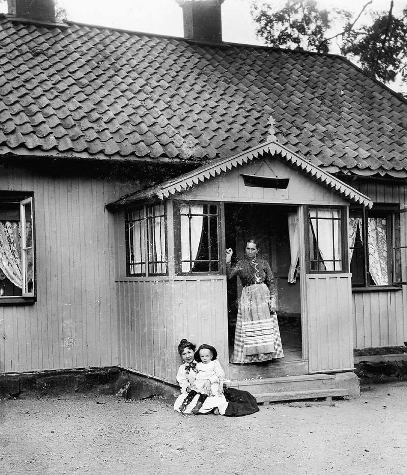 Tre personer framför ett trähus med lite snickarglädje.