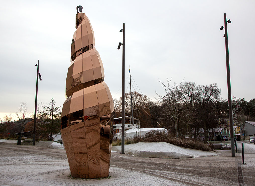 Guldig hög skulptur med en öppning. Skulpturen står på ett torg.