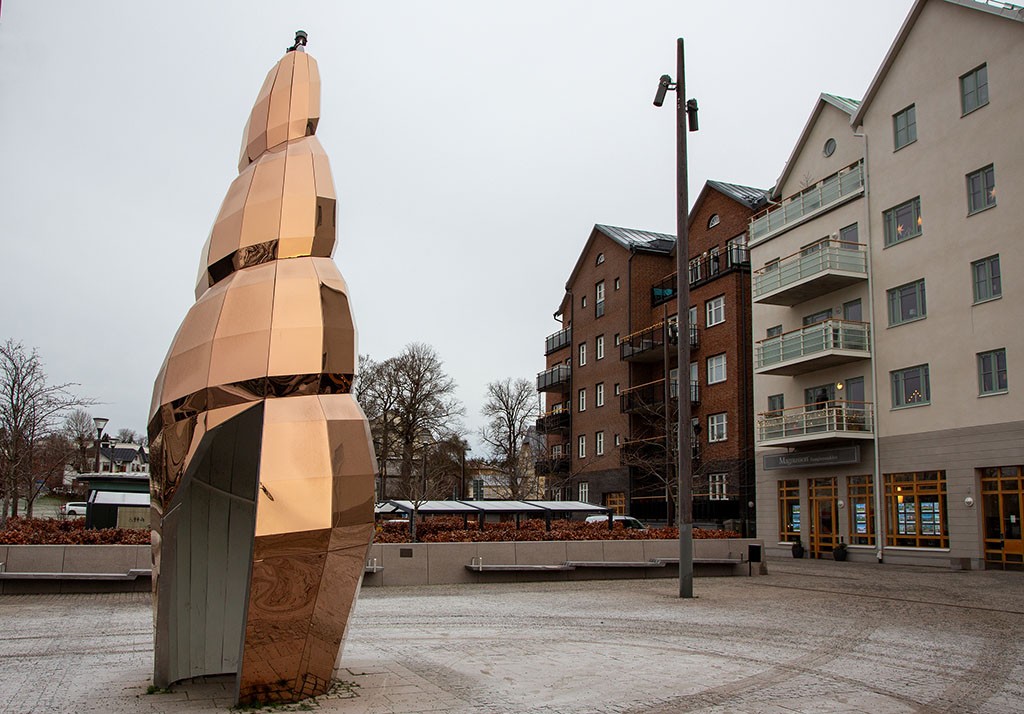 Guldig hög skulptur med en öppning. Skulpturen står på ett torg.