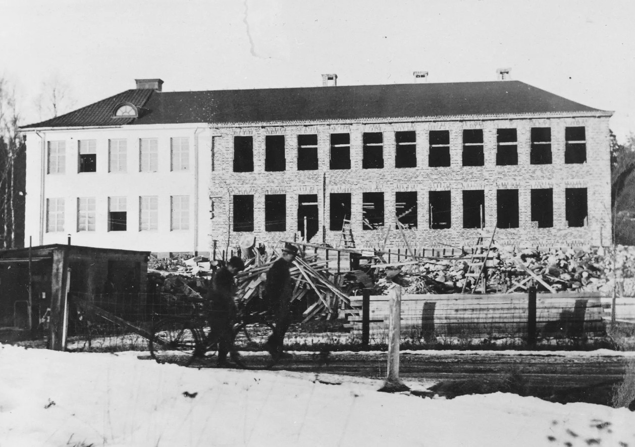 En svartvit bild av skolan med tillbyggnaden med tomma fönstergluggar.